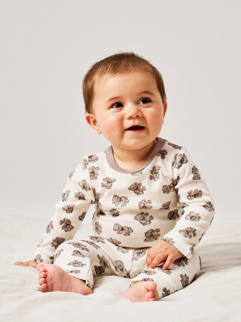 Baby i et kremfarget langermet todelt sett med brunt teddybjørnmønster og brun halskant.