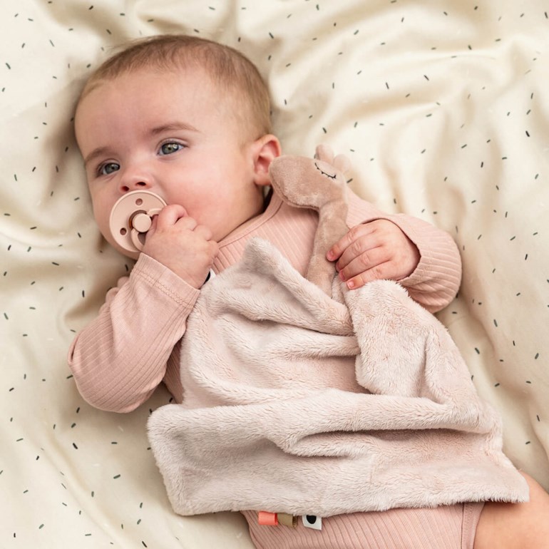 Baby har på seg en støvrosa ribbet langermet body, holder et matchende kosedyr og en rosa smokk.
