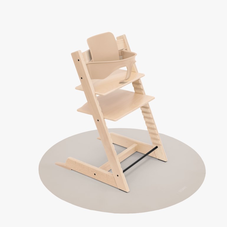 Lys trehøystol med et beige babysett står på en rund lys grå matte.