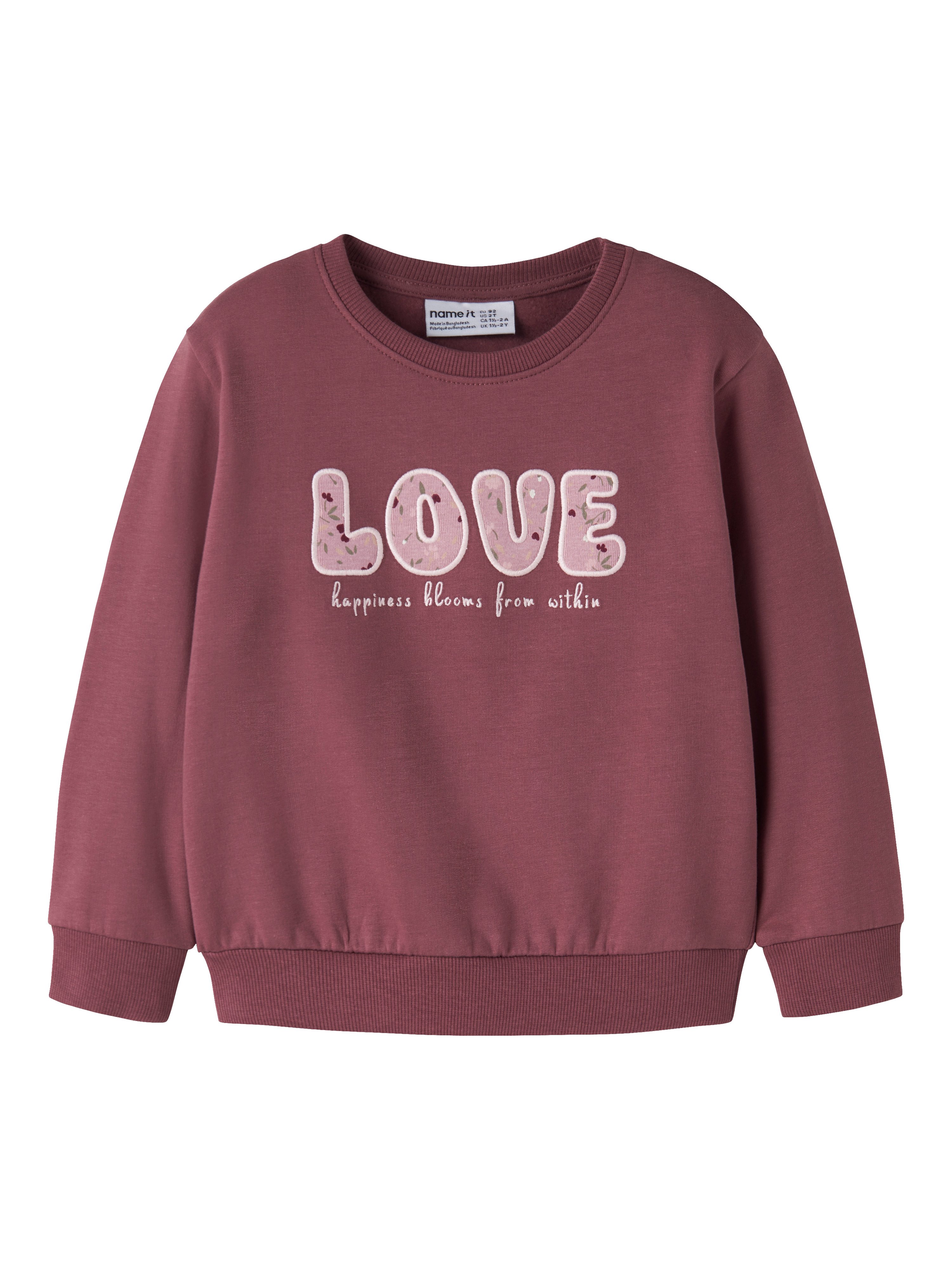 Barnas mauve genser framfra med blomstrete 'LOVE'-trykk og inspirerende tekst under.