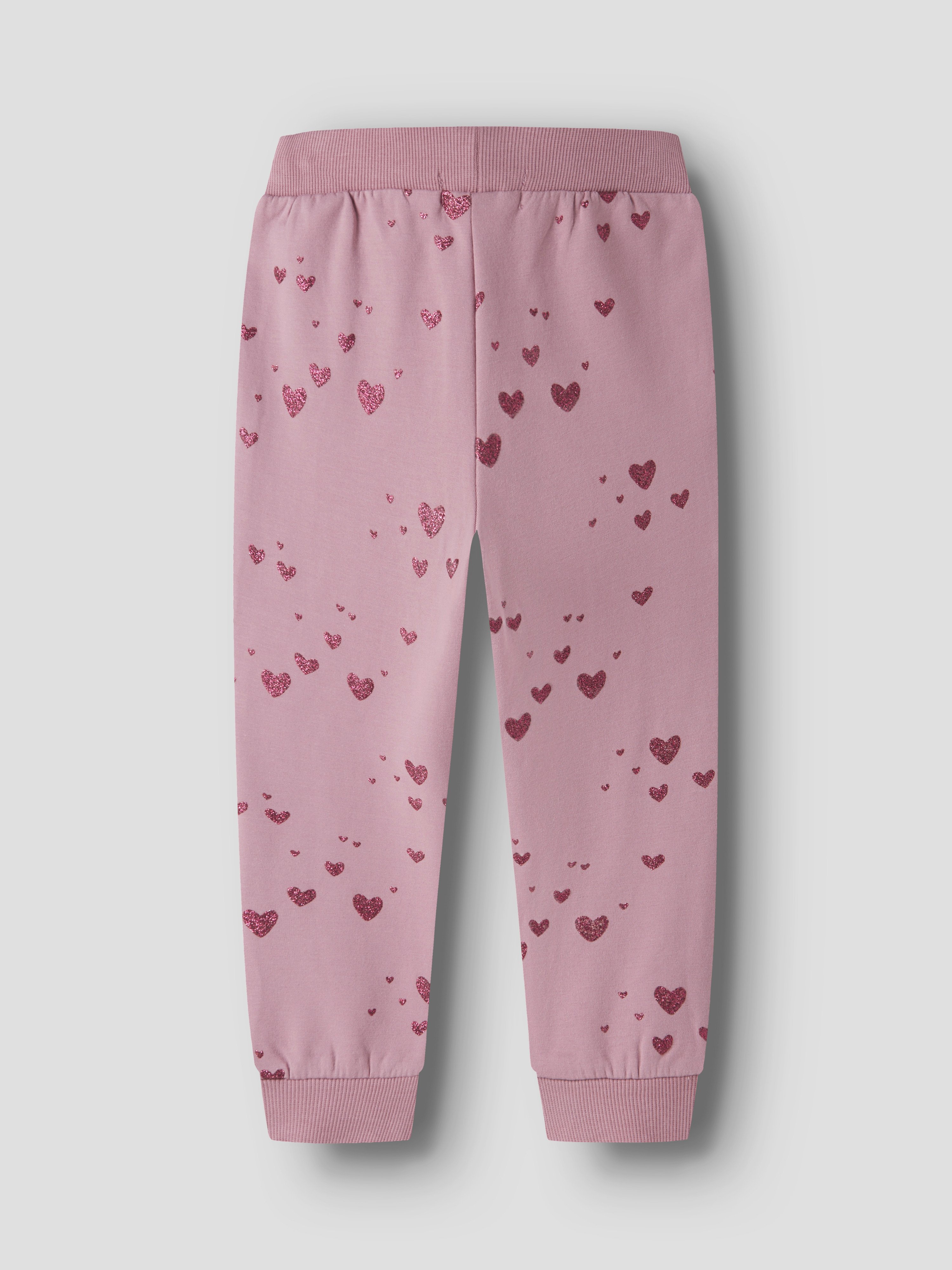 Barns rosa joggebukse med heldekkende glitrende hjertemønster, elastisk linning og ribbestrikkede mansjetter, forfra.