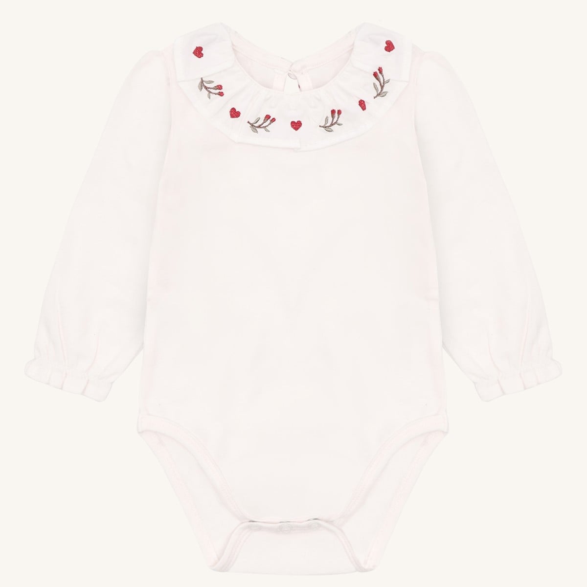 Hvit babybody med lange ermer og en volangkrage brodert med røde hjerter og grønne kvister.