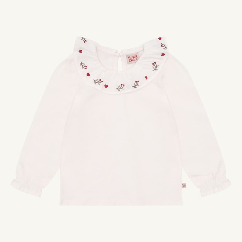 Hvit langermet barnetopp med volangkrave brodert med røde hjerter og blomstermotiver, og volangmansjetter.