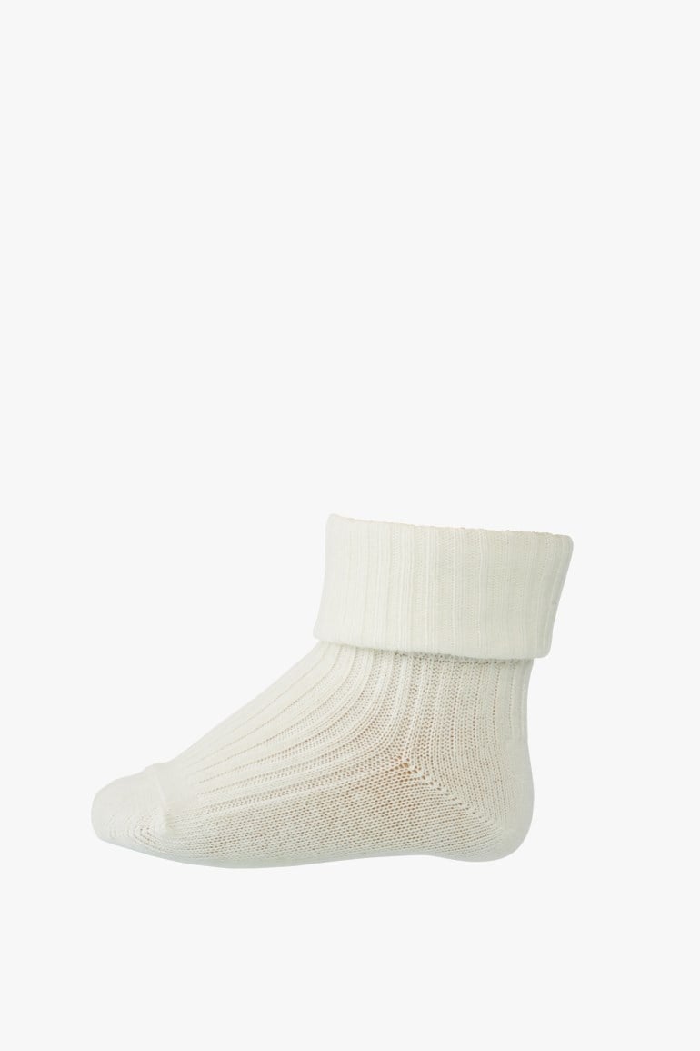 En hvit ribbestrikket babystrømpe med brettet mansjett.