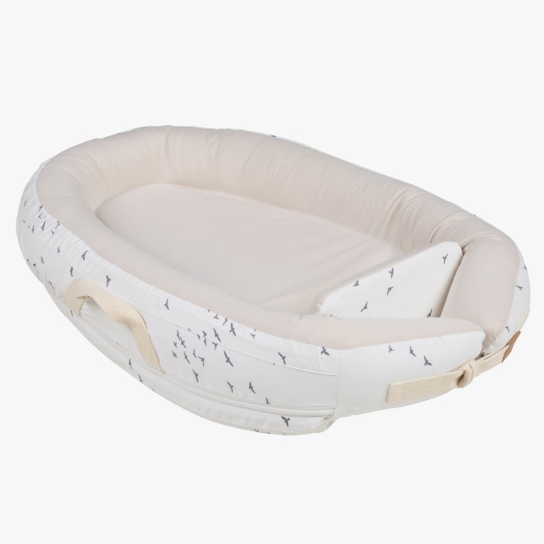 En offwhite babynest med grått fuglemønster og lys beige innside, med håndtak på sidene.