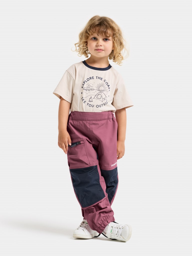 Kid's tofargede støvrosa og marineblå utebukser, elastisk midje, med beige grafisk t-skjorte og hvite sneakers.
