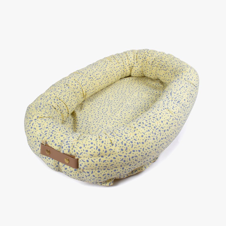 Ovalt gult babynest med blått flekkete mønster og brunt lær håndtak.
