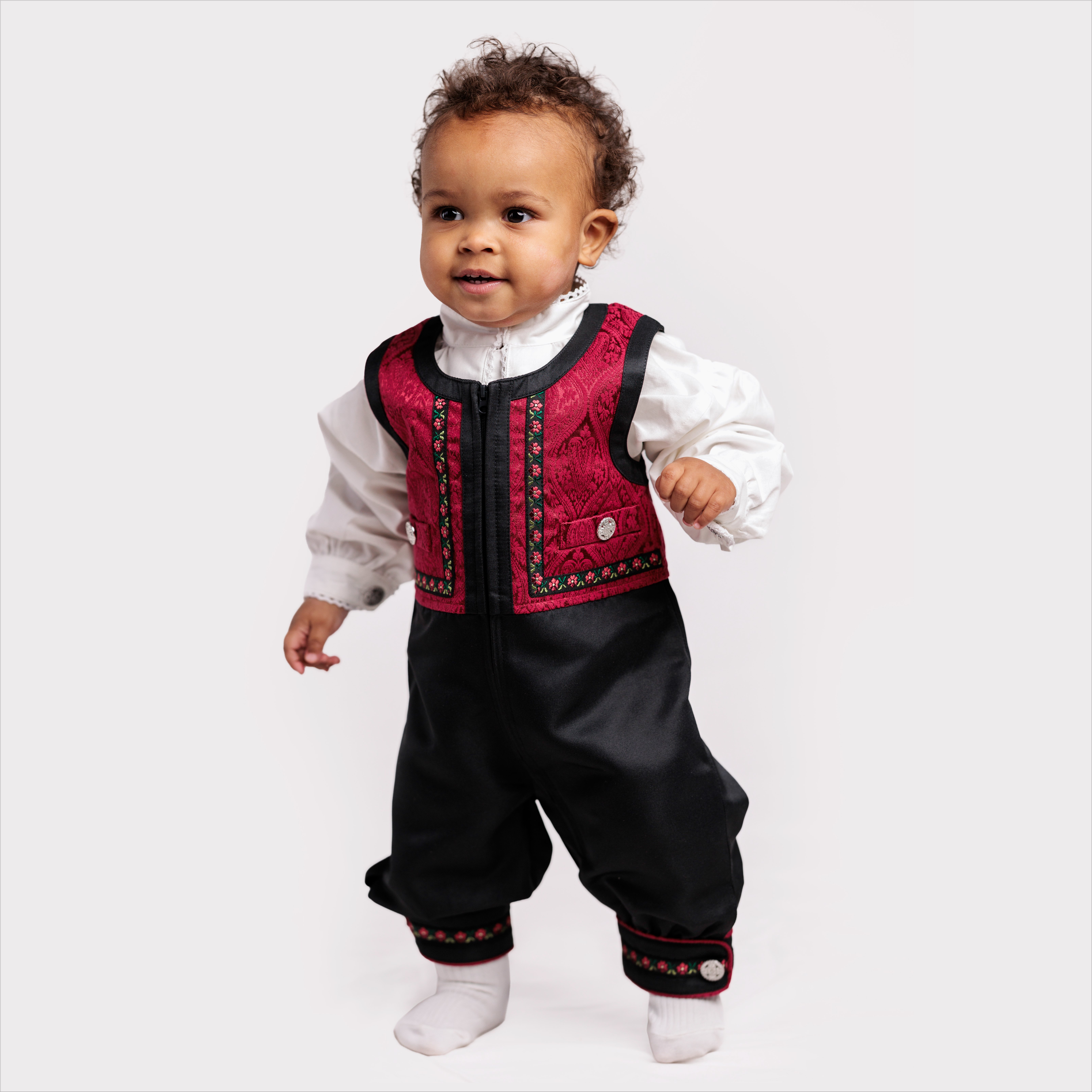 Babyens svart og rødbrodert vest og bukser antrekk med hvit skjorte og hvite sokker.