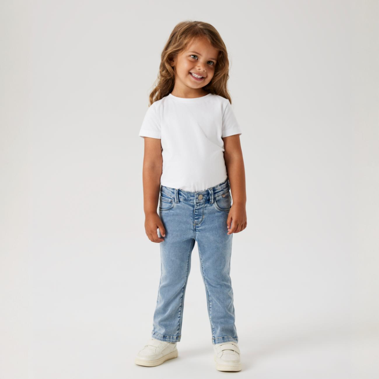 Barn iført lyseblåe slim-fit jeans, en hvit kortermet t-skjorte og hvite sneakers, forfra.