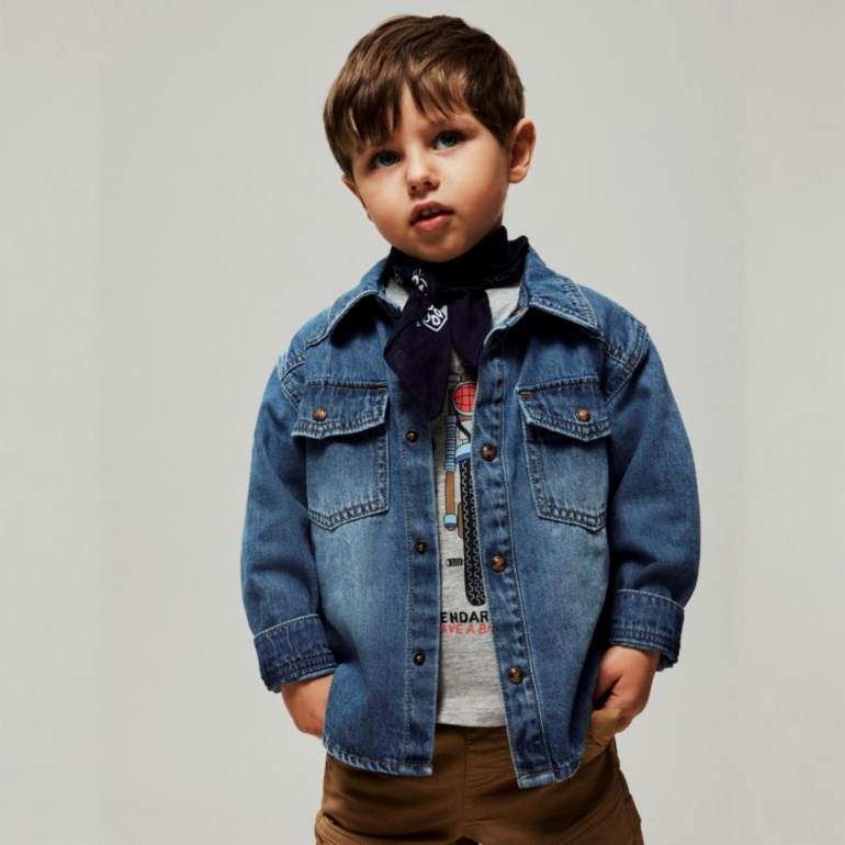 Gutt i blå dongeriskjorte med brystlommer over en grå t-skjorte, mørkblå bandana og brune bukser.