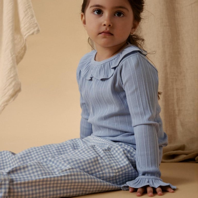 Barn i lys blå ribbestrikket langermet topp med rysjekrage og mansjetter, og blårutete bukser.