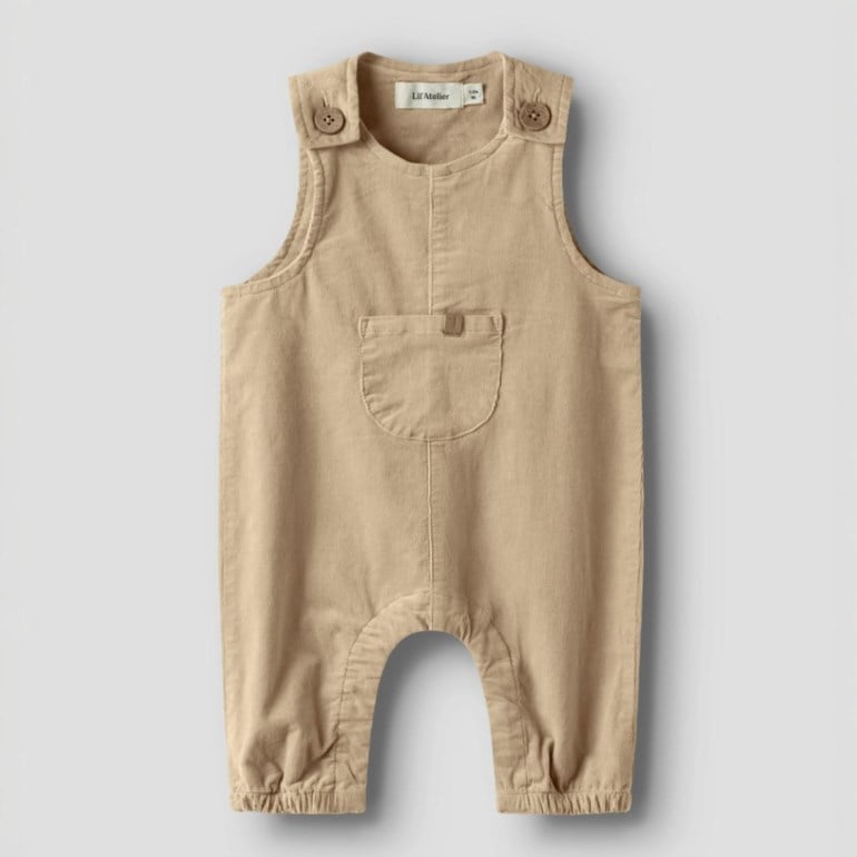 Frontvisning av en baby lysbrun cordfløyel-overall med skulderknapper, brystlomme og elastiske ankler.