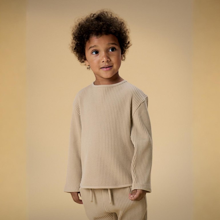 Barn i beigefarget ribbet langermet topp og matchende ribbet joggebukse, forfra.