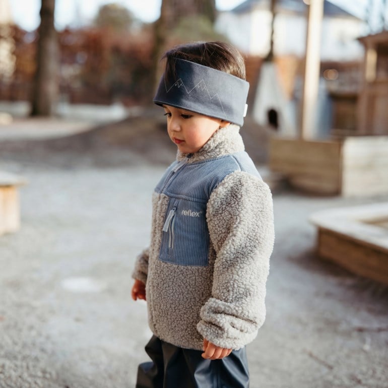 Barn i grå sherpafleece halv-zip jakke med blå kordfløyel, mørkegrått fjellpannebånd og mørke bukser.