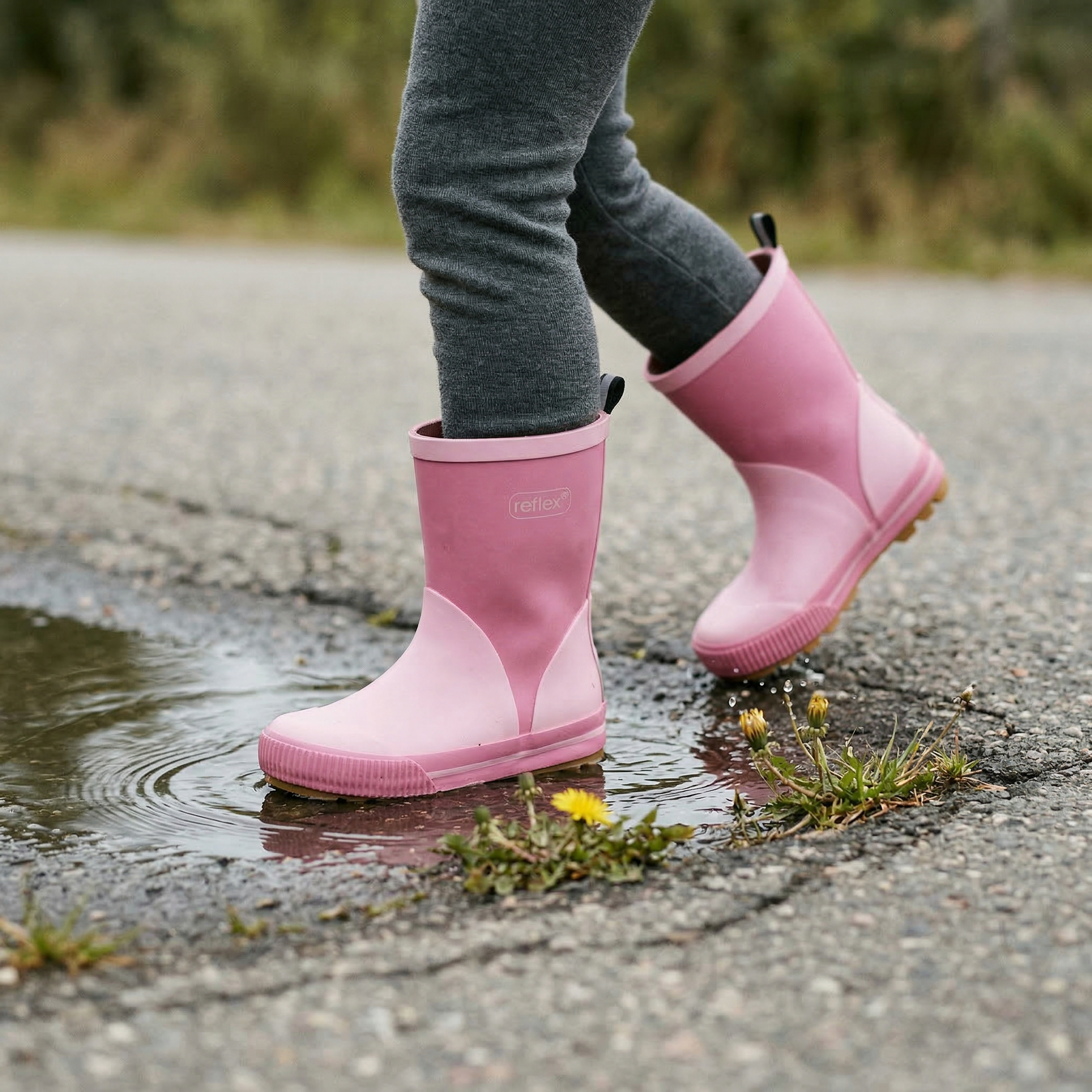 Barn iført tofargede rosa gummistøvler og grå leggings, tråkker i en sølepytt.