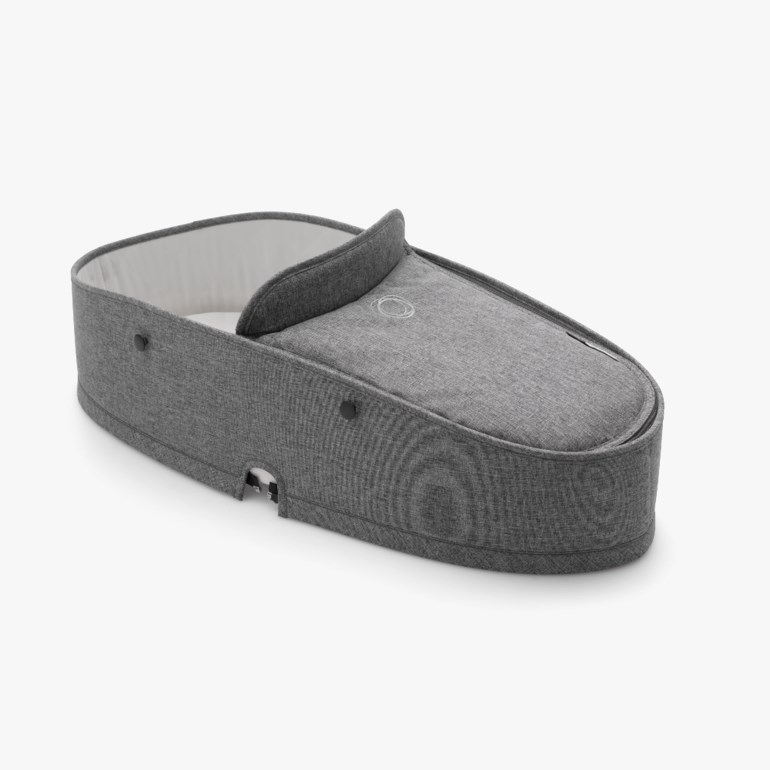 Grå stoff babybag med hvit foring og avtakbart trekk, med svarte trykknapper og utskjæringer i bunnen.