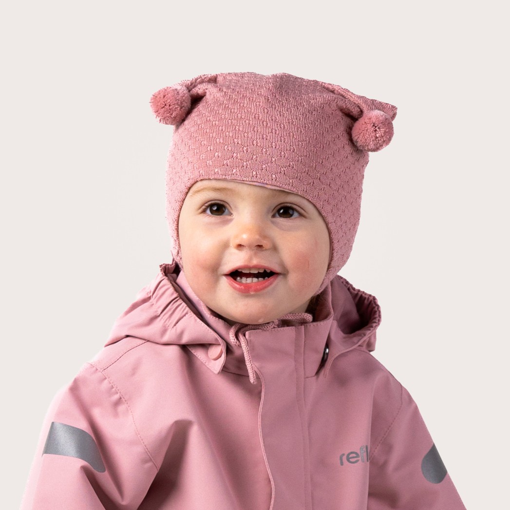 Baby i rosa strikket lue med dusker og teksturert mønster, samt en rosa hettejakke med refleksdetaljer.
