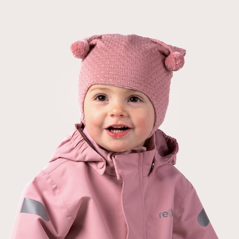 Baby i rosa strikket lue med dusker og teksturert mønster, samt en rosa hettejakke med refleksdetaljer.