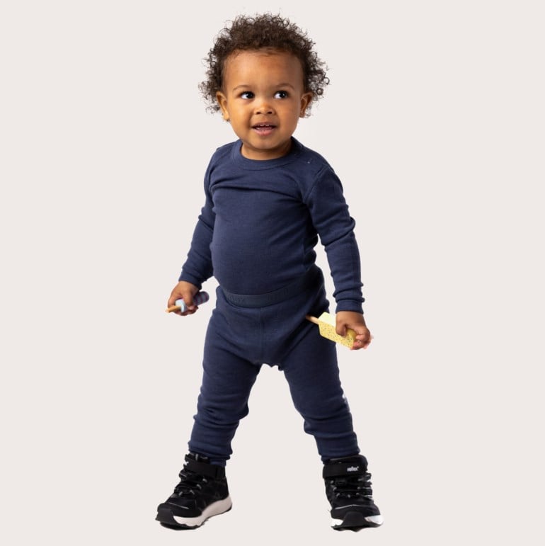 Baby har på seg mørkblå langermet termotopp og matchende termoleggings, svarte sko, holder to leker.